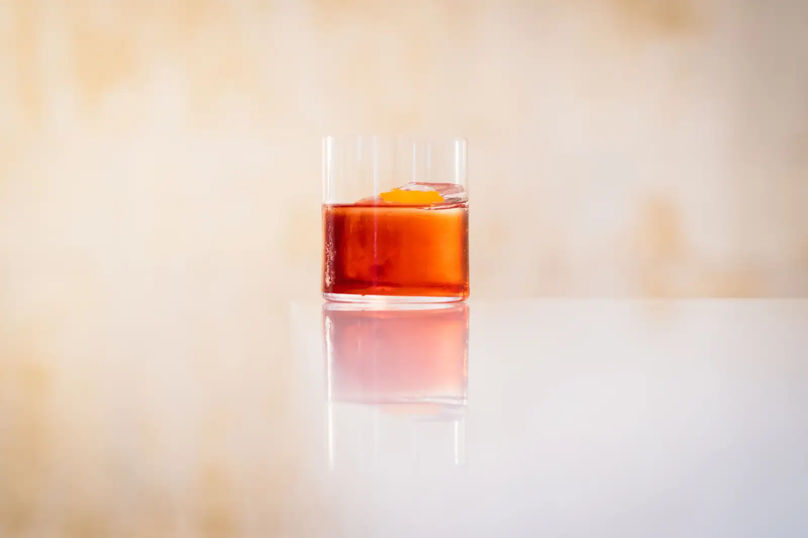 Cocktail italien rouge dans un verre bas, gros glaçon unique et zeste d'orange posé dessus