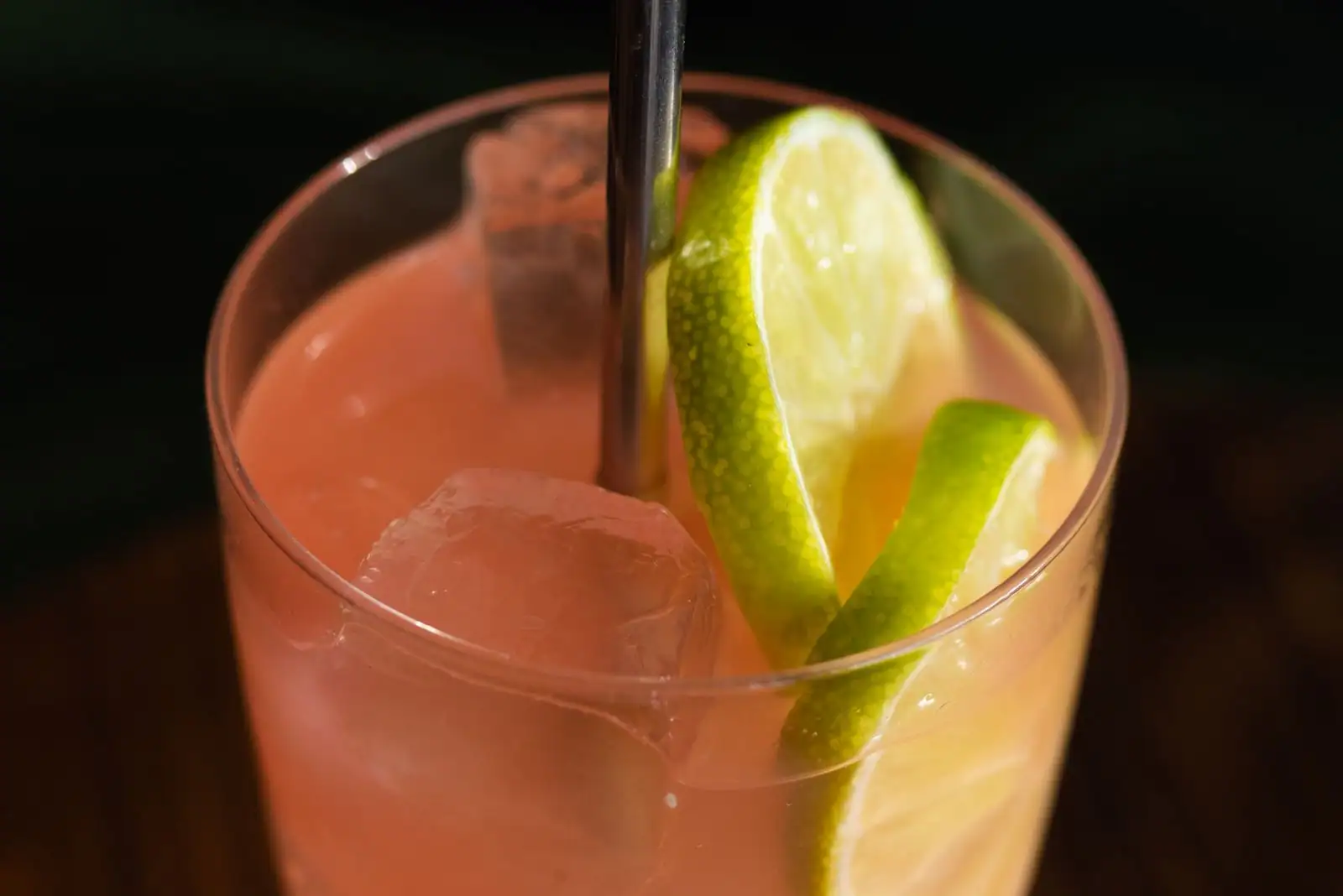 Cocktail rose aux agrumes servi sur de gros glaçons, deux quartiers de citron vert dans le verre