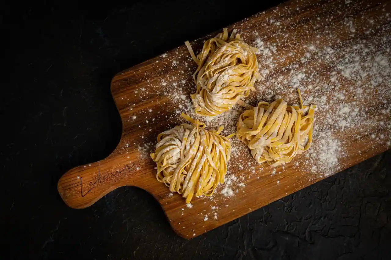 Trois nids de tagliatelle fraîches aux œufs saupoudrés de farine sur une planche en bois