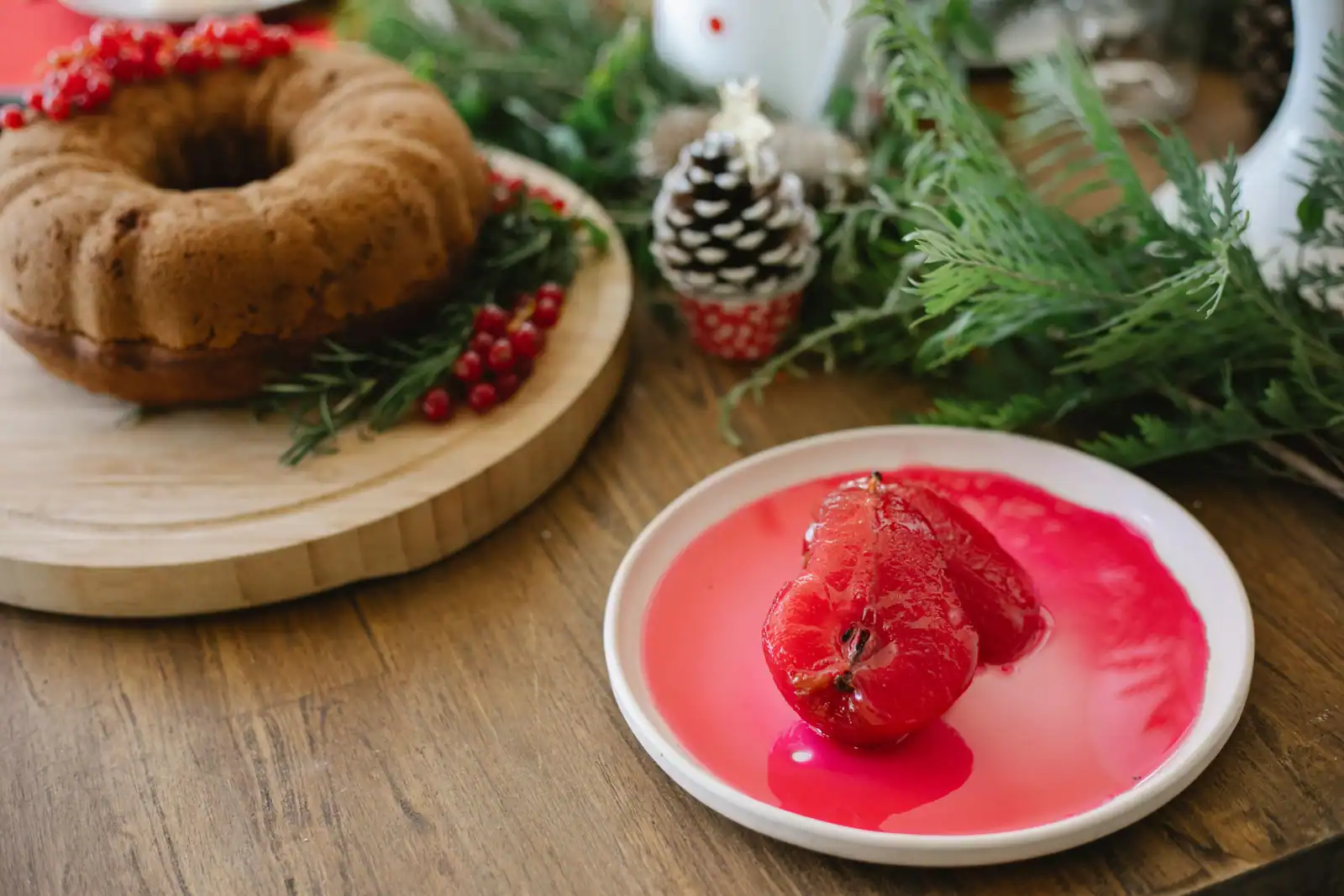 Poire pochée dans un sirop rouge servie à l'assiette, près d'un gâteau et de branchages de Noël