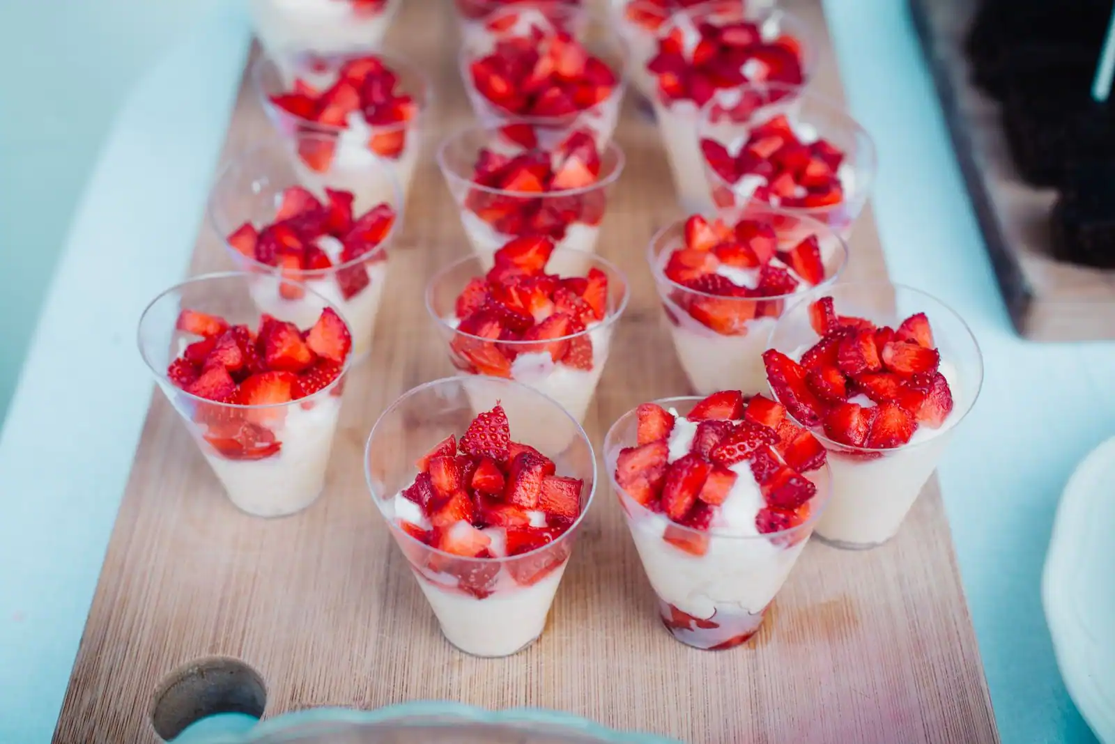 Verrines de fraises et de crème alignées sur une planche en bois, prêtes à servir dehors