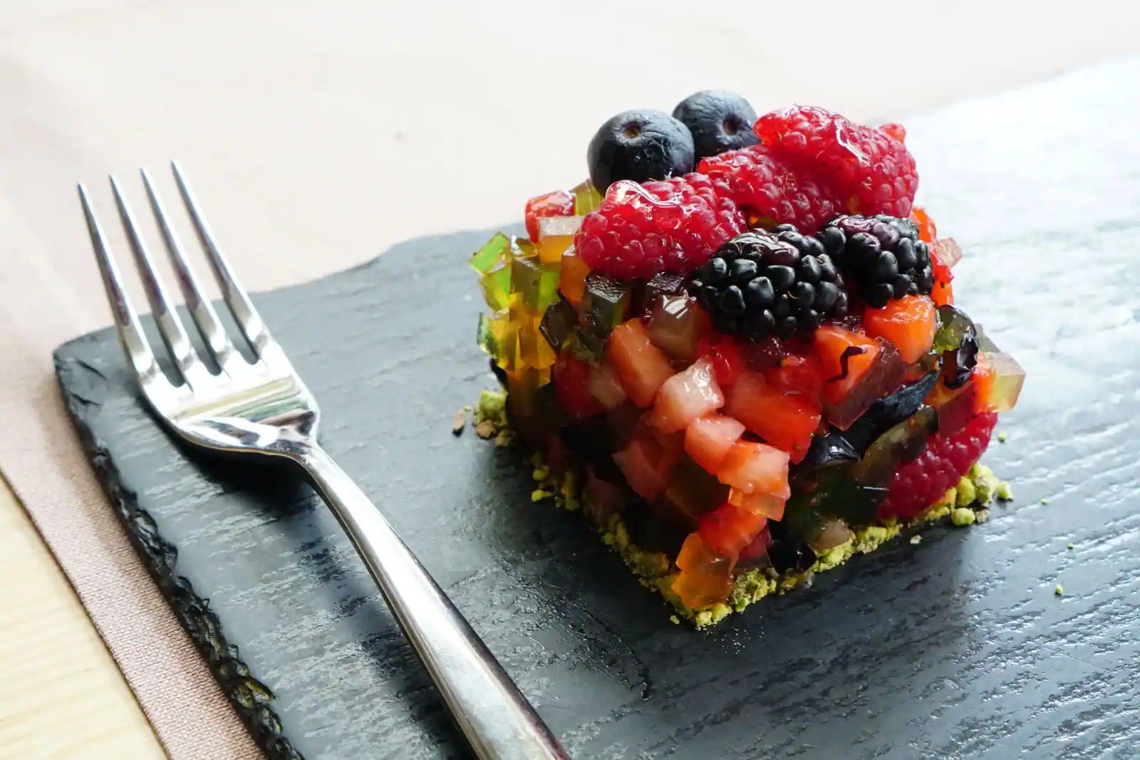 Dessert dressé en cube sur une ardoise, garni de framboises, de mûres et de myrtilles