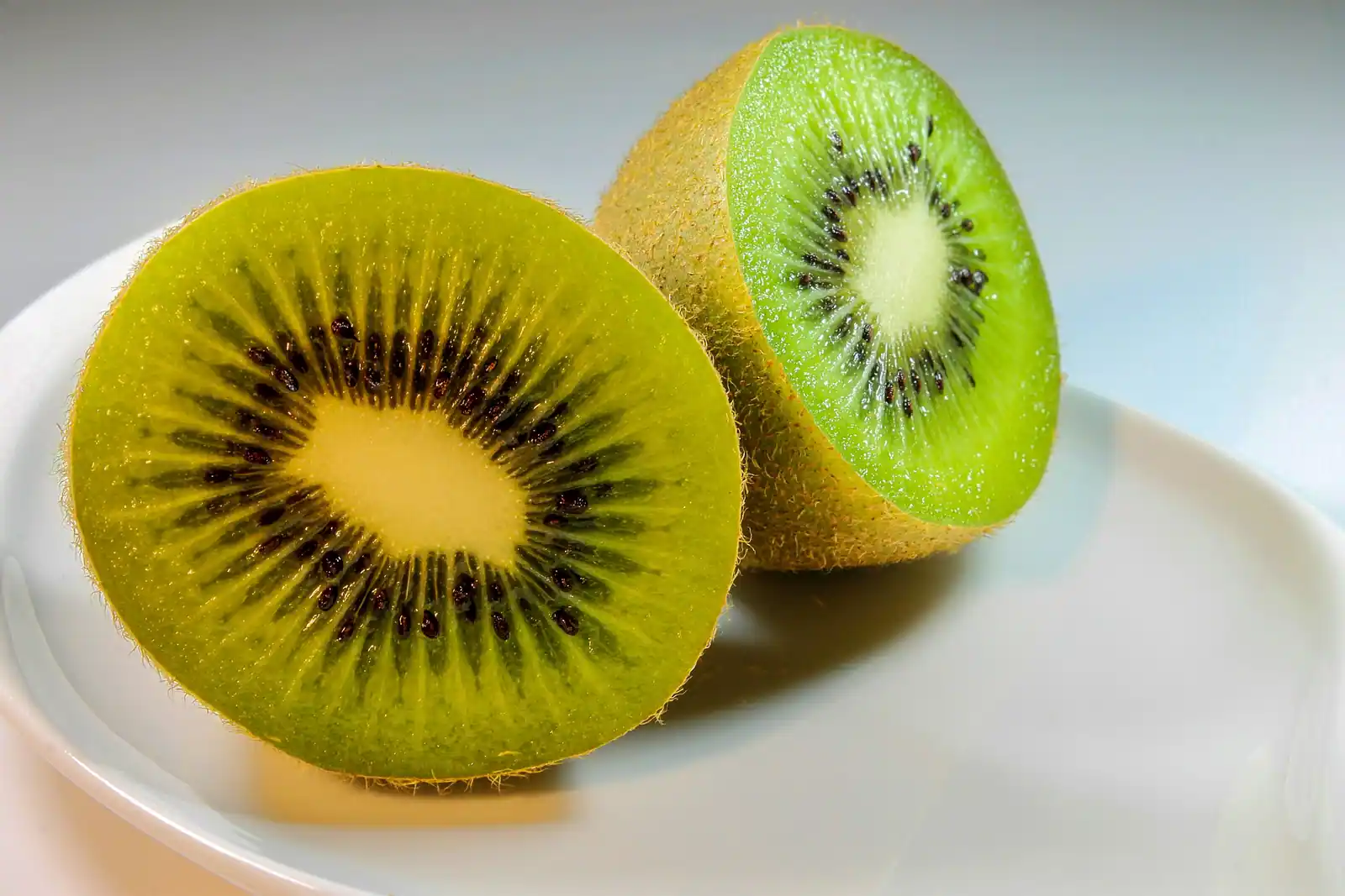 Deux moitiés de kiwi vert posées dans une assiette blanche, chair verte et graines noires visibles.