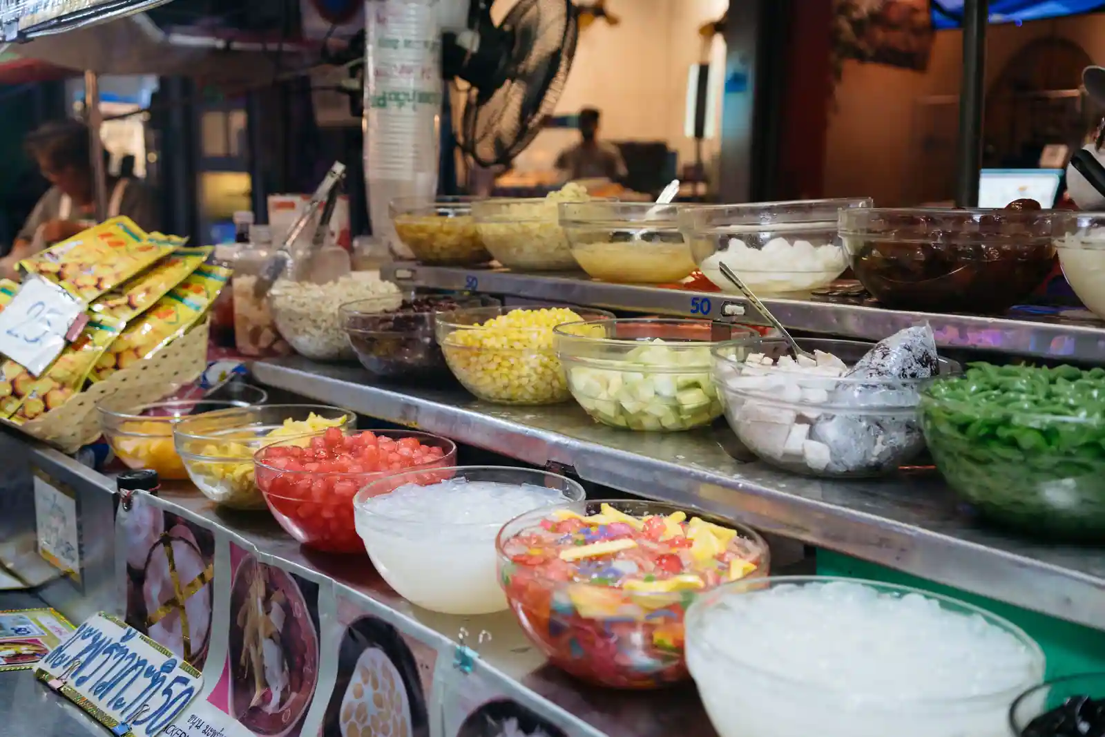 Étal de desserts thaïlandais : bols de verre remplis de gelées colorées, de maïs, de coco et de glace