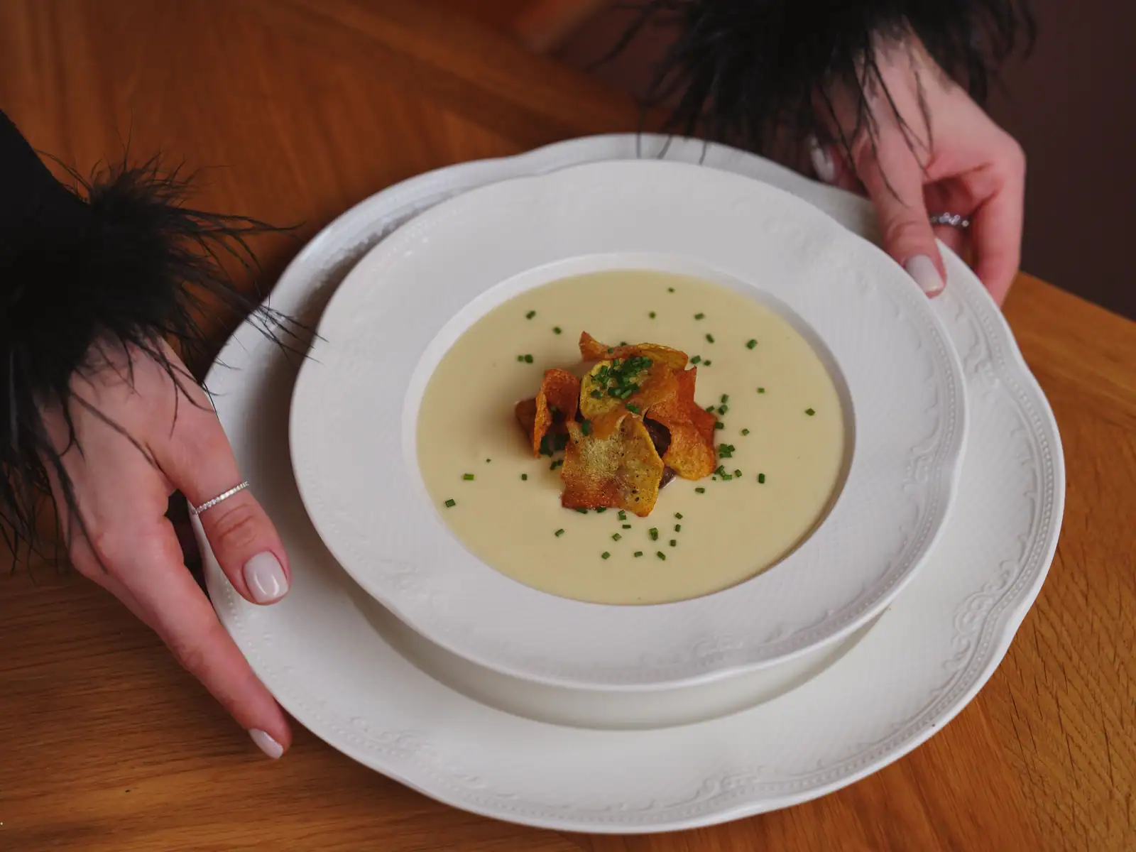 Velouté servi en assiette creuse de porcelaine blanche, garni de chips de légume et de ciboulette.