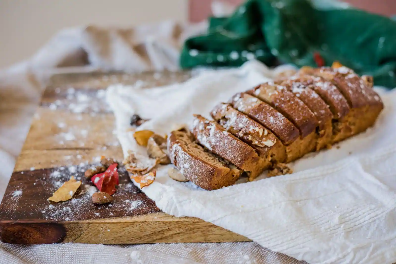 Cake maison tranché sur une planche en bois, parsemé de sucre glace et d'éclats de fruits secs