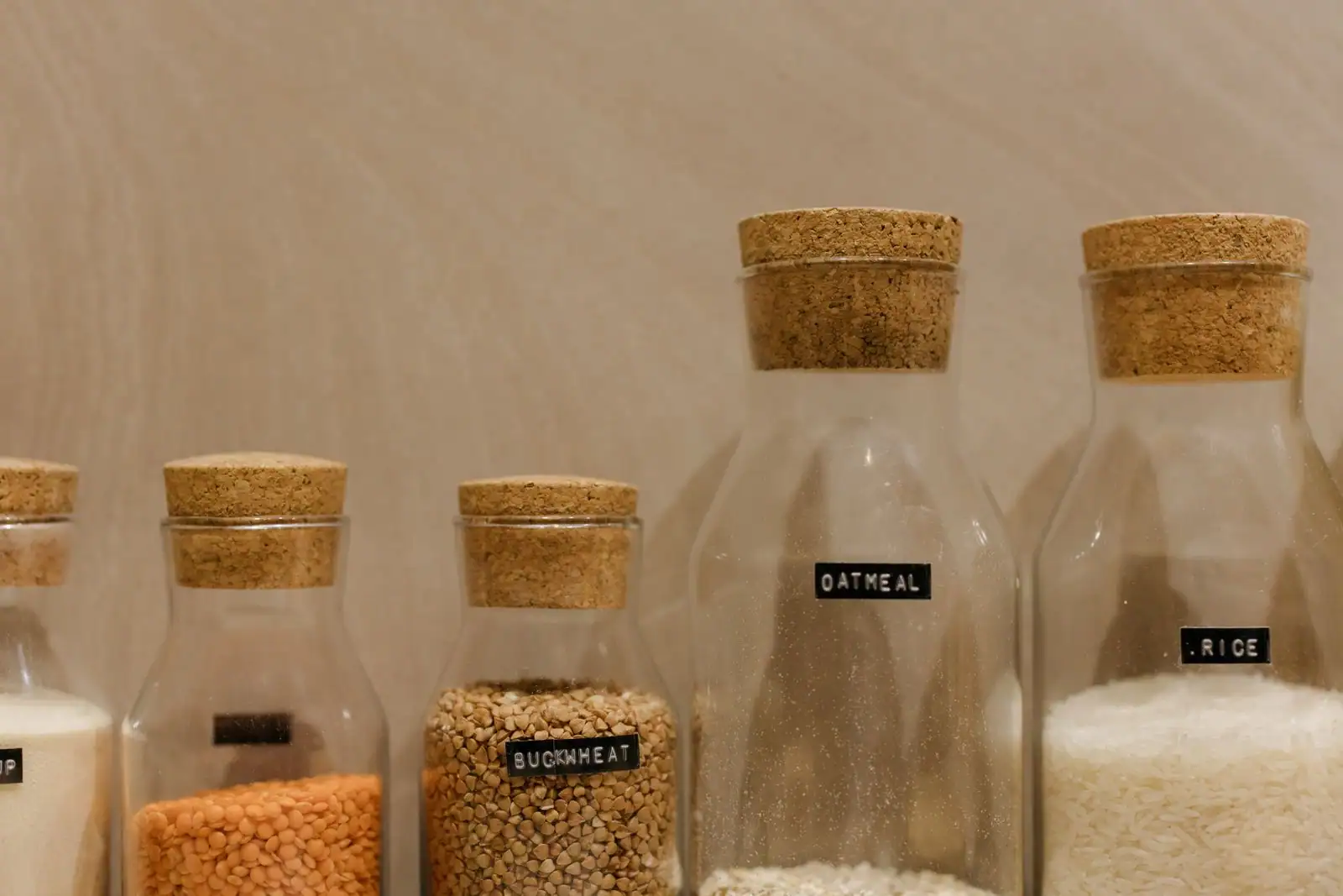 Bocaux en verre étiquetés contenant sarrasin, riz et lentilles, alignés sur une étagère de cuisine
