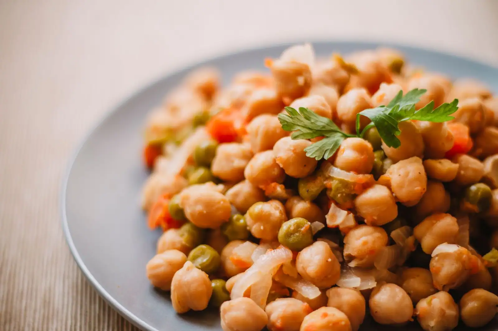 Assiette de pois chiches mijotés aux petits pois, carottes et oignons, garnie de persil frais
