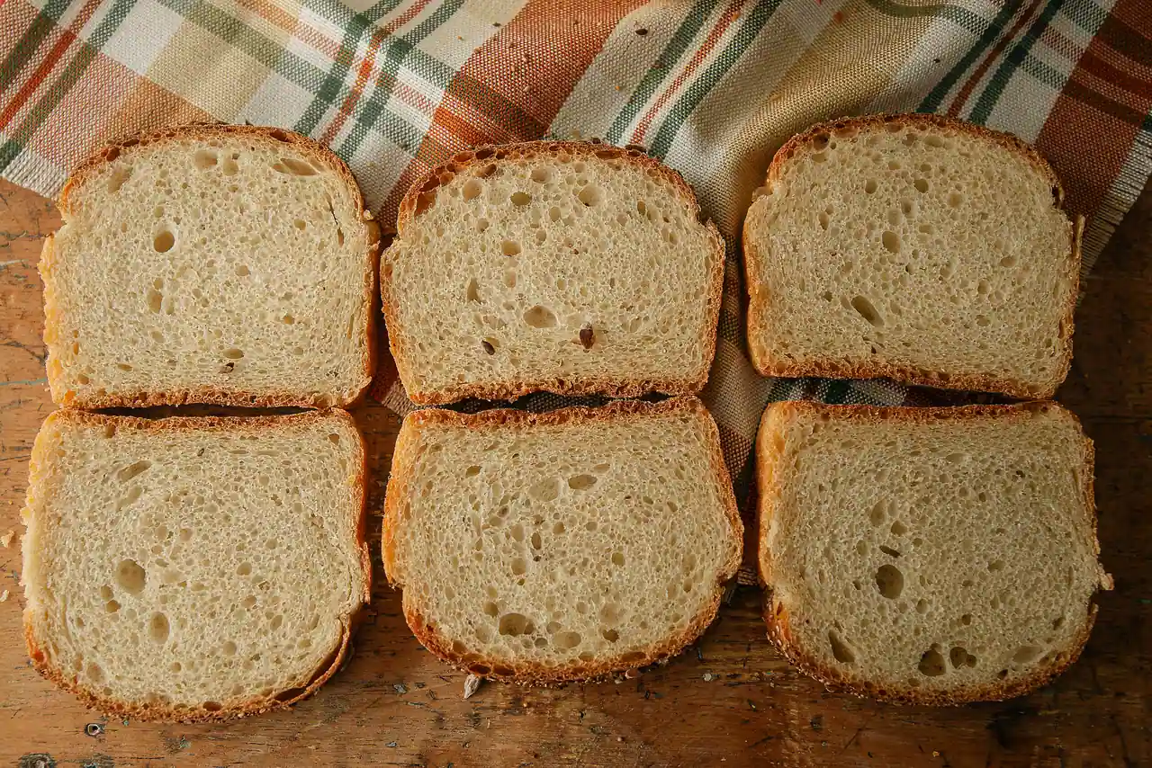Six tranches de pain de mie à la mie fine et serrée, alignées sur une table en bois