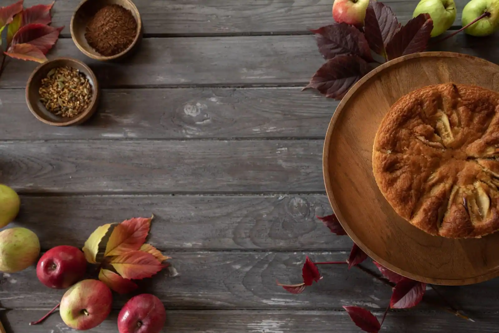 Gâteau aux pommes rond garni de quartiers en rosace, sur un plateau en bois entouré de pommes