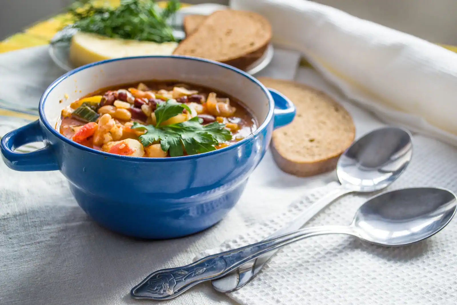 Soupe de légumes non mixée aux haricots blancs et rouges, servie en bol bleu avec du pain.