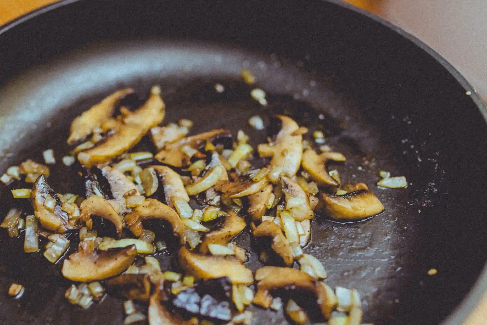 Champignons émincés et oignons qui dorent dans une poêle, vus de près pendant la coloration