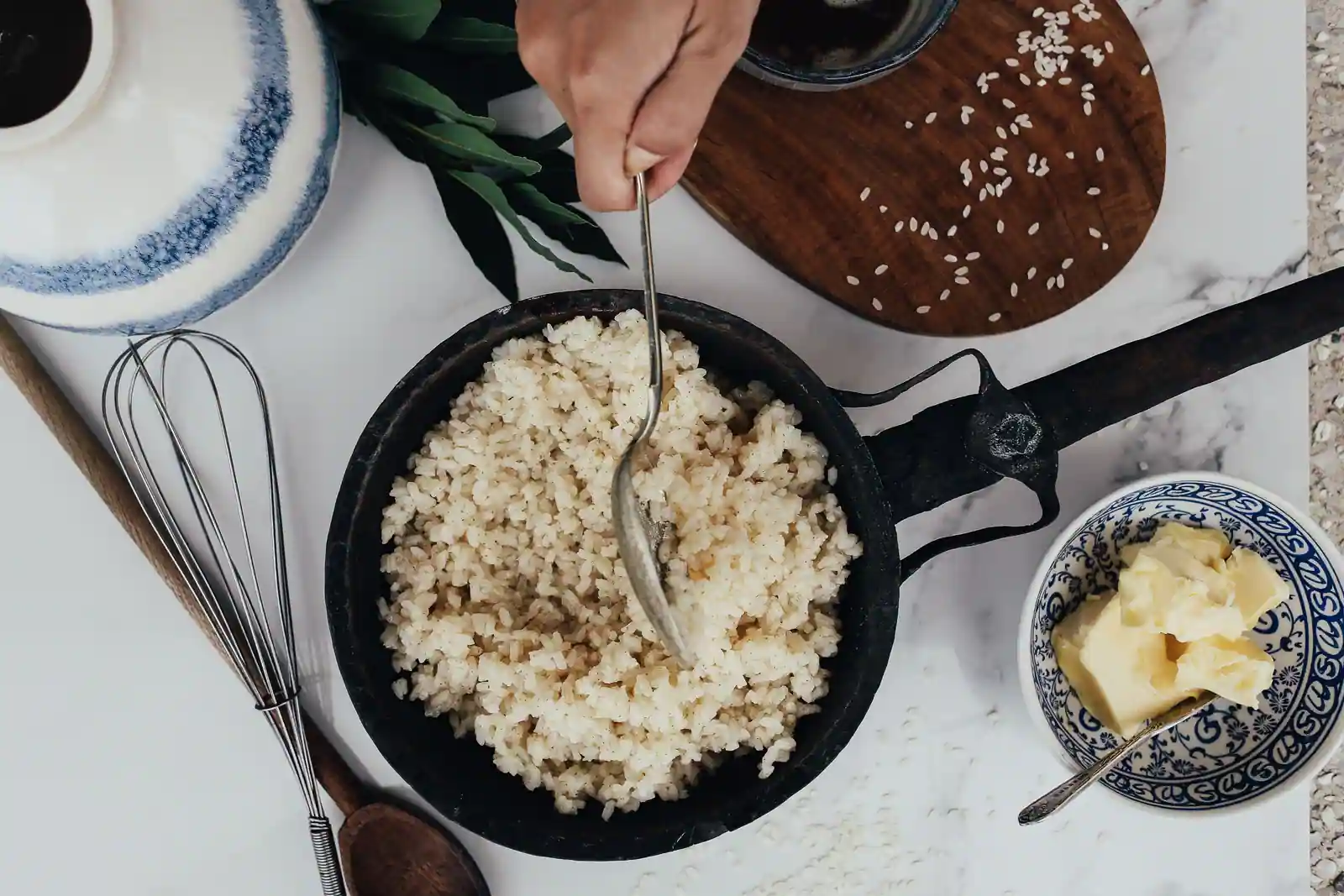 Riz rond cuit dans une petite poêle en fonte, avec du beurre, des grains crus et une cuillère en bois.