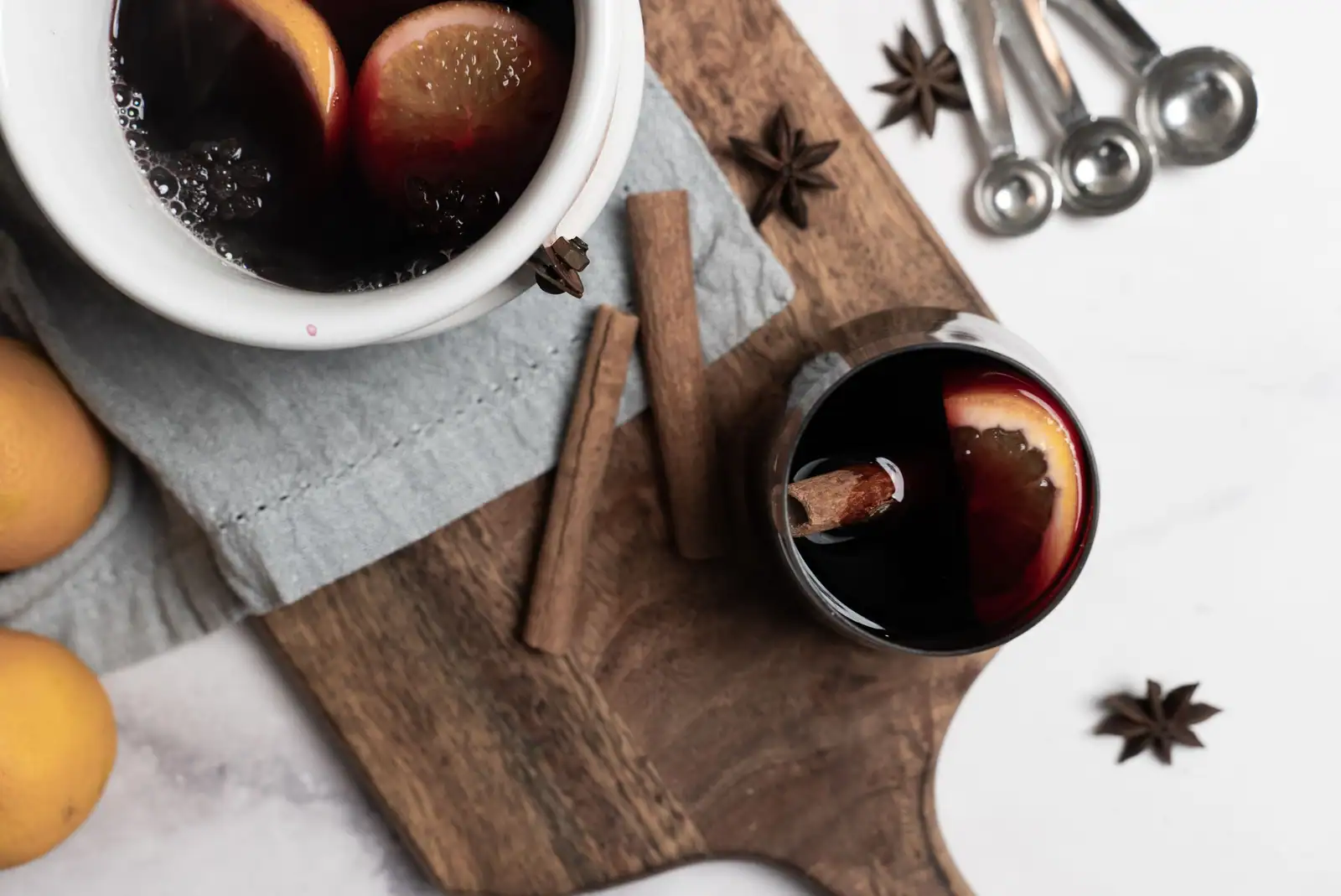 Cocotte et verre de vin chaud aux agrumes, avec bâtons de cannelle, badiane et cuillères doseuses