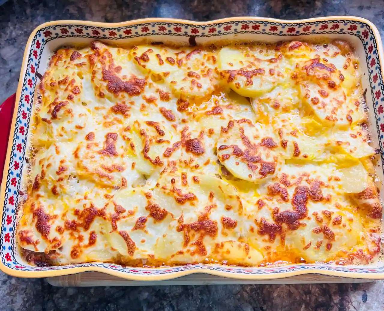 Gratin de pommes de terre à la croûte de fromage doré, dans un plat en céramique à motif fleuri.