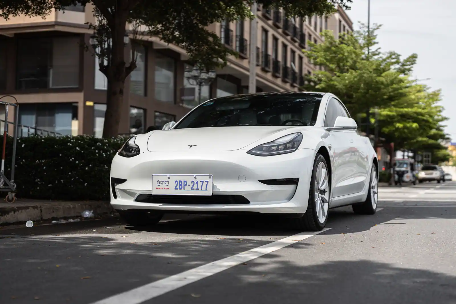 Tesla Model 3 blanche garée le long d'un trottoir, avant et pare-brise du véhicule bien visibles